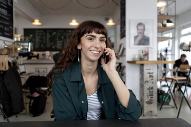 Smiling young woman on cell phone in a cafe - FLLF00071