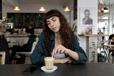 Young woman with milky coffee sitting at table in a cafe - FLLF00072