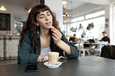 Young woman with milky coffee sitting at table in a cafe - FLLF00073