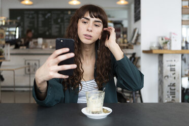 Junge Frau benutzt Mobiltelefon in einem Café - FLLF00076