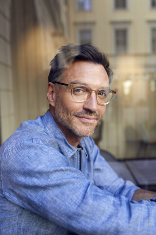 Porträt eines selbstbewussten Mannes mit Brille hinter einer Fensterscheibe, lizenzfreies Stockfoto