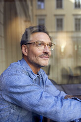 Portrait of man wearing glasses behind windowpane - PNEF01413