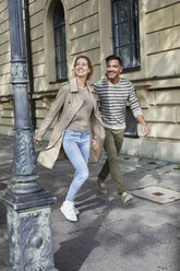 Happy couple walking on pavement in the city - PNEF01421