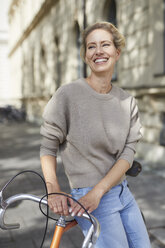 Porträt einer glücklichen Frau mit Fahrrad in der Stadt - PNEF01428