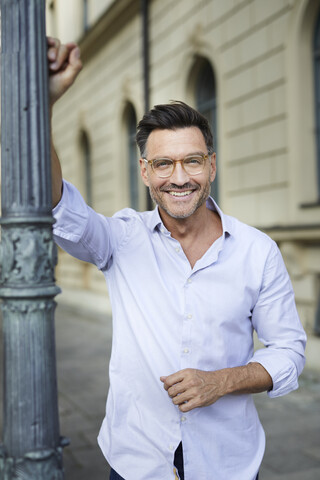 Portrait of smiling businessman leaning against lamp post in the city stock photo