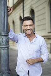 Portrait of smiling businessman leaning against lamp post in the city - PNEF01436