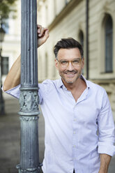 Portrait of smiling businessman leaning against lamp post in the city - PNEF01437