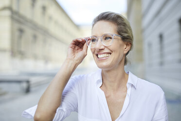 Porträt einer lächelnden Frau mit weißem Hemd und Brille in der Stadt - PNEF01458