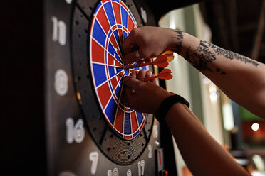 Nahaufnahme eines tätowierten Mannes, der Darts aus einer elektronischen Dartscheibe nimmt - ZEDF02026