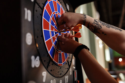 Nahaufnahme eines tätowierten Mannes, der Darts aus einer elektronischen Dartscheibe nimmt - ZEDF02026