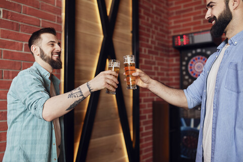 Two happy friends clinking beer glasses at dartboard in a pub stock photo