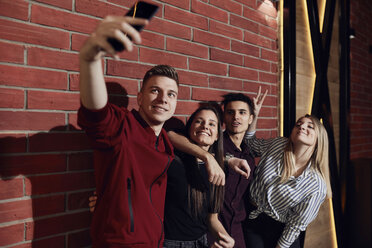Happy friends taking a selfie with smartphone at brick wall - ZEDF02074