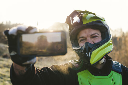 Porträt eines Motocross-Fahrers, der bei Sonnenuntergang ein Selfie macht - FBAF00340