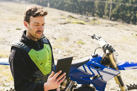 Porträt eines Motocross-Fahrers mit Blick auf ein Tablet, lizenzfreies Stockfoto