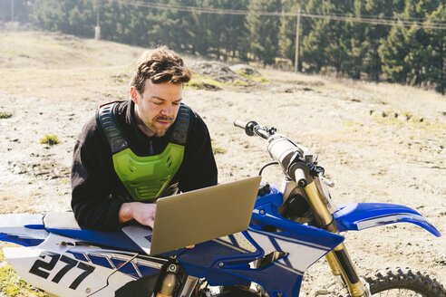 Porträt eines Motocross-Fahrers mit Laptop - FBAF00350