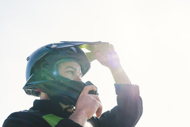 Porträt eines Motocross-Fahrers, der bei Sonnenuntergang seinen Helm aufsetzt - FBAF00354