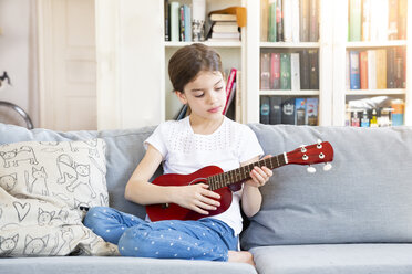 Porträt eines Mädchens, das zu Hause auf der Couch sitzt und Ukulele spielt - LVF07926