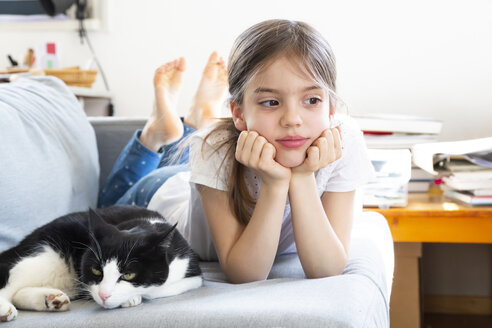Porträt eines kleinen Mädchens, das mit einer Katze auf der Couch liegt - LVF07929