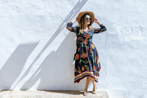 Spanien, Cadiz, Vejer de la Frontera, modische Frau mit Strohhut vor weißer Wand stehend - KIJF02448