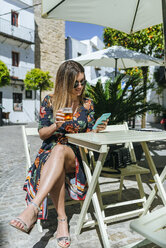 Spanien, Cadiz, Vejer de la Frontera, junge Frau sitzt in einem Straßencafé mit einem Glas Bier und schaut auf das Telefon - KIJF02469