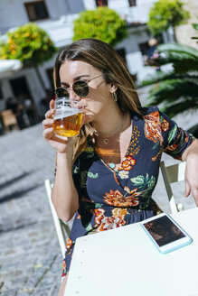 Spanien, Cadiz, Vejer de la Frontera, junge Frau sitzt in einem Straßencafé und trinkt ein Glas Bier - KIJF02471