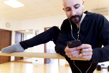 Balletttänzerin dehnt sich und benutzt ihr Handy im Ballettstudio - FMOF00462