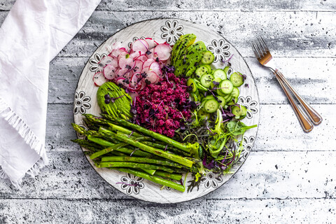Frühlingshafter Salatteller mit grünem Spargel, rotem Quinoa, Avocado, roten Radieschen, Gurke und Sprossen, lizenzfreies Stockfoto