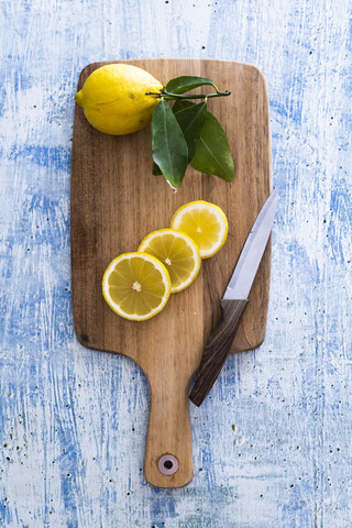 Zitronenscheiben und ganze Zitrone auf Holzbrett mit Küchenmesser, lizenzfreies Stockfoto