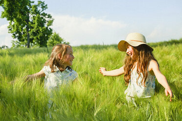 Happy, carefree sisters in sunny, idyllic rural green wheat field - FSIF03792