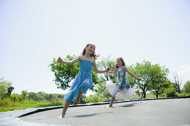 Playful, carefree barefoot girls in dresses playing on trampoline in sunny backyard - FSIF03793