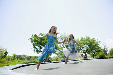 Verspielt, sorglos barfuß Mädchen in Kleidern spielen auf Trampolin in sonnigen Hinterhof - FSIF03793