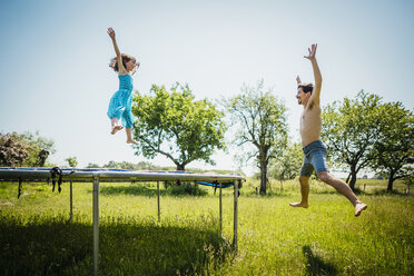 Playful father and daughter jumping on trampoline in sunny summer back yard - FSIF03794