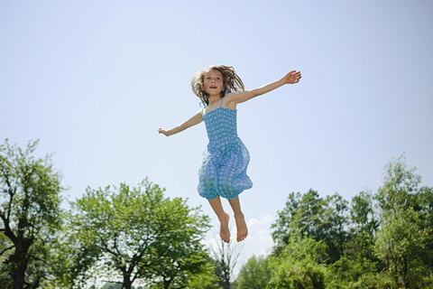 Unbekümmertes Mädchen im Kleid springt vor Freude im sonnigen Hinterhof, lizenzfreies Stockfoto