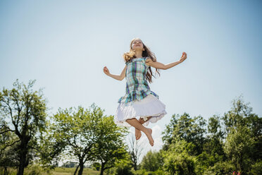 Unbekümmertes Mädchen im Kleid springt vor Freude im sonnigen Hinterhof - FSIF03802
