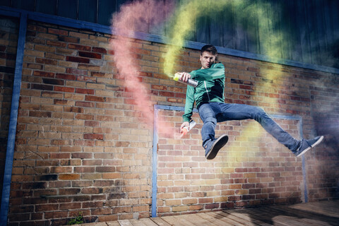 Porträt männlicher moderner Tänzer, der mit Sprühfarbe gegen eine Ziegelwand tanzt, lizenzfreies Stockfoto