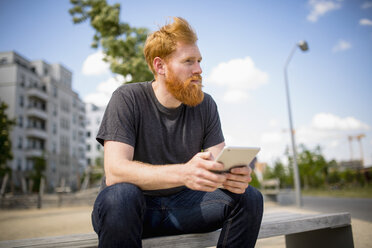 Hipster-Mann mit Bart, der ein digitales Tablet auf einer städtischen Bank benutzt - FSIF03846