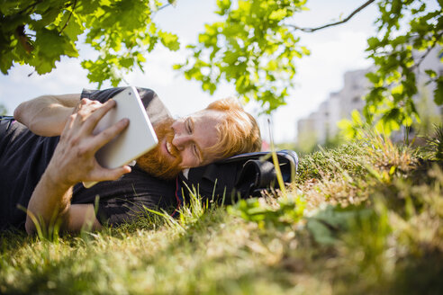 Lächelnder Mann mit Bart, der in einem sonnigen Park ein digitales Tablet benutzt - FSIF03851