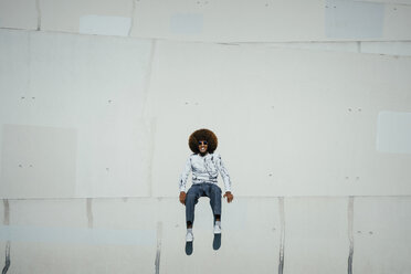 Porträt glücklicher junger Mann mit Afro an der Wand sitzend - FSIF03867