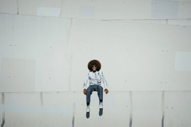 Portrait happy young man with afro sitting on wall - FSIF03867