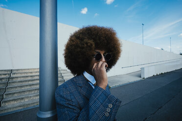 Gut gekleideter junger Mann mit Afro, der auf einem städtischen Bürgersteig eine Zigarette raucht - FSIF03872