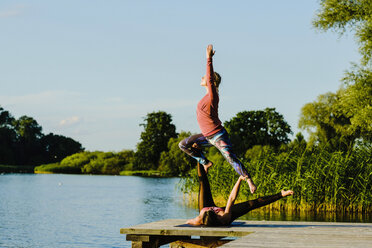 Frauen üben Acroyoga auf einem sonnigen Steg am See - FSIF03885