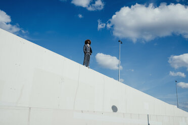Cooler, gut gekleideter junger Mann mit Afro auf einer sonnigen Stadtmauer stehend - FSIF03891