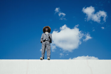 Confident, cool, well-dressed young man with afro standing on sunny wall against blue sky - FSIF03892