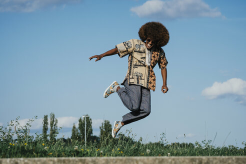 Unbekümmerter junger Mann mit Afro, der vor Freude springt - FSIF03897
