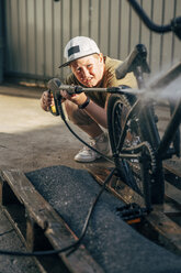 Junge wäscht BMX-Fahrrad mit Hochdruckreiniger auf dem Hof - VPIF01187