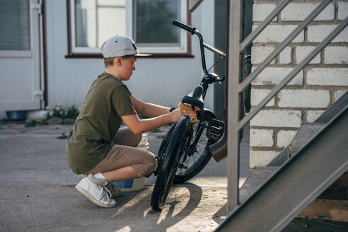 Boy cleaning bmx bike on yard - VPIF01190