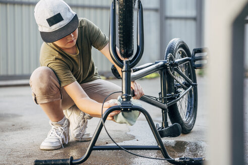 Boy cleaning bmx bike on yard - VPIF01195