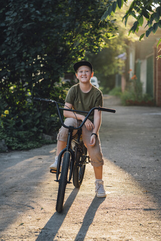 Porträt eines lächelnden Jungen mit BMX-Fahrrad auf der Straße, lizenzfreies Stockfoto