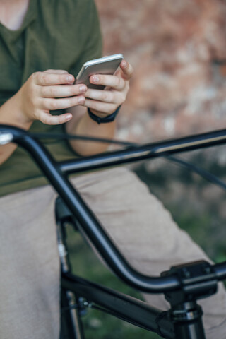 Nahaufnahme eines Jungen mit BMX-Fahrrad, der ein Mobiltelefon benutzt, lizenzfreies Stockfoto