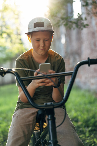 Junge mit BMX-Fahrrad, der ein Mobiltelefon benutzt, lizenzfreies Stockfoto